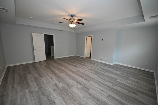 empty room featuring a raised ceiling, ceiling fan, and light hardwood / wood-style floors