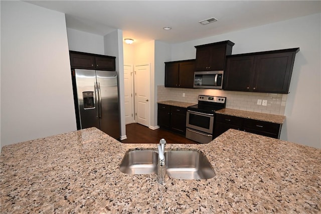 kitchen featuring dark brown cabinetry, light stone countertops, sink, tasteful backsplash, and appliances with stainless steel finishes