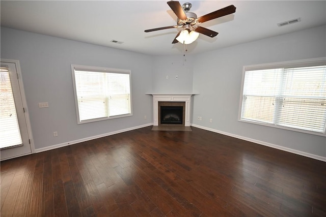 unfurnished living room featuring a tile fireplace, a wealth of natural light, dark wood-type flooring, and ceiling fan