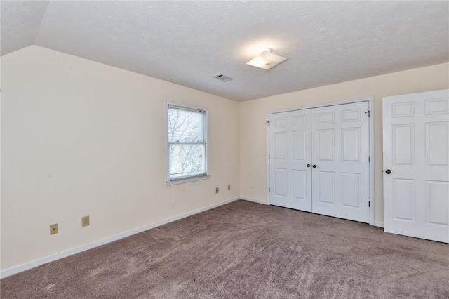 unfurnished bedroom with lofted ceiling, carpet flooring, a textured ceiling, and a closet