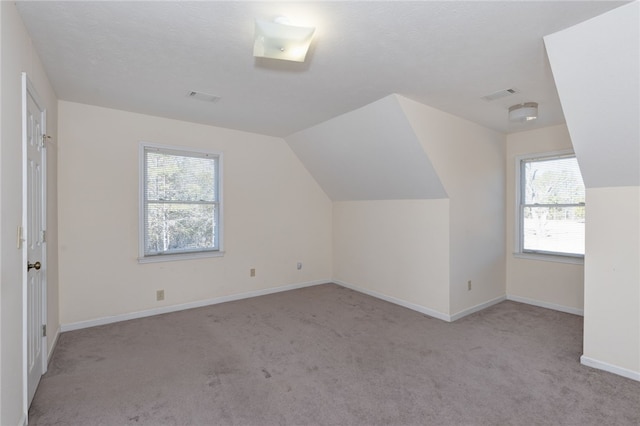 bonus room with plenty of natural light, vaulted ceiling, and light carpet