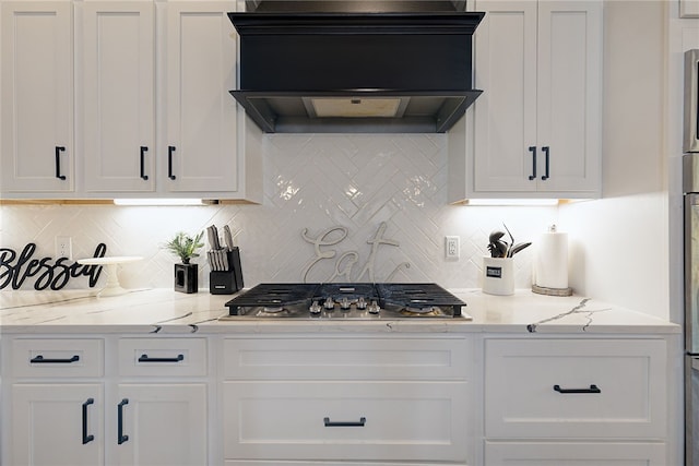 kitchen featuring light stone counters, stainless steel gas cooktop, white cabinets, backsplash, and custom exhaust hood