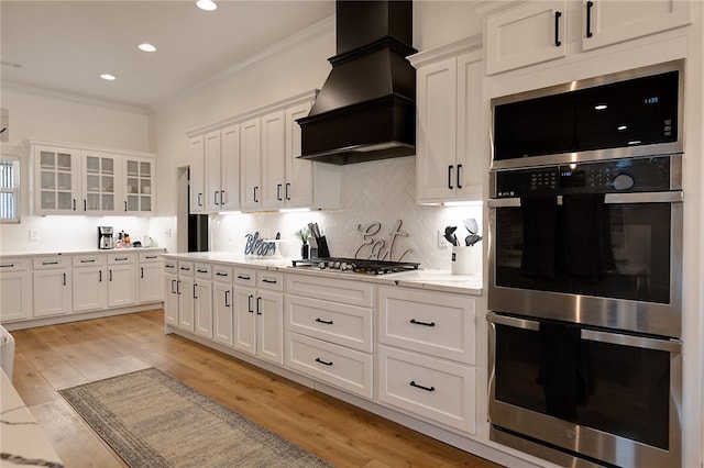 kitchen with glass insert cabinets, white cabinetry, appliances with stainless steel finishes, and custom exhaust hood