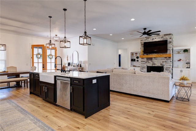 kitchen with light countertops, hanging light fixtures, stainless steel dishwasher, open floor plan, and a kitchen island with sink