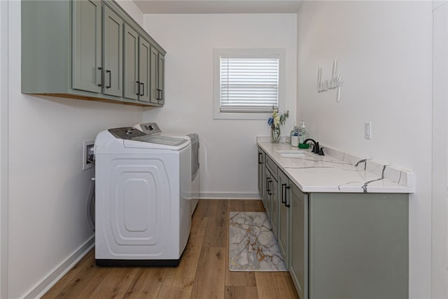 washroom featuring cabinet space, light wood-style flooring, a sink, washer and dryer, and baseboards