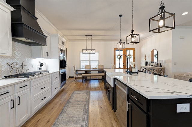 kitchen with a center island with sink, premium range hood, white cabinetry, pendant lighting, and a sink