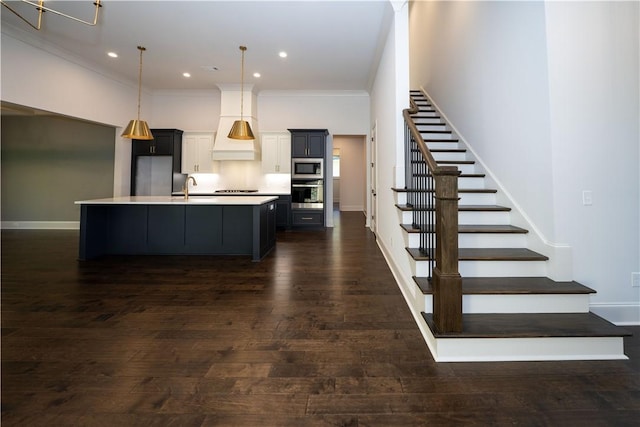 kitchen with sink, stainless steel appliances, pendant lighting, a center island with sink, and custom exhaust hood