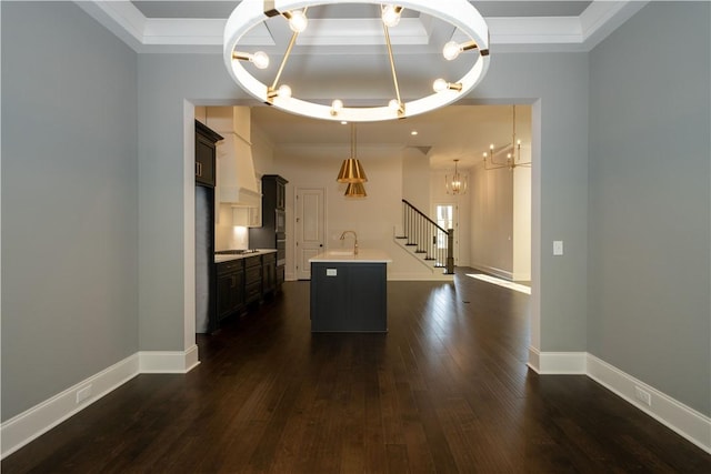 kitchen with ornamental molding, dark wood-type flooring, sink, a center island with sink, and hanging light fixtures