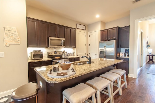 kitchen featuring sink, stainless steel appliances, a breakfast bar area, decorative backsplash, and a center island with sink