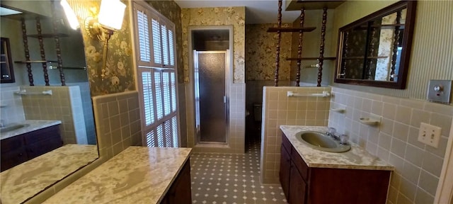 full bath with a wainscoted wall, two vanities, a stall shower, a sink, and tile walls