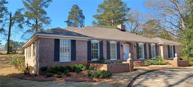 view of front facade featuring brick siding, a chimney, and a shingled roof