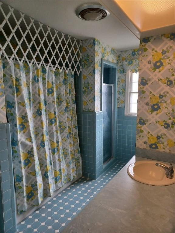 full bathroom with a wainscoted wall, a shower stall, wallpapered walls, and tile walls