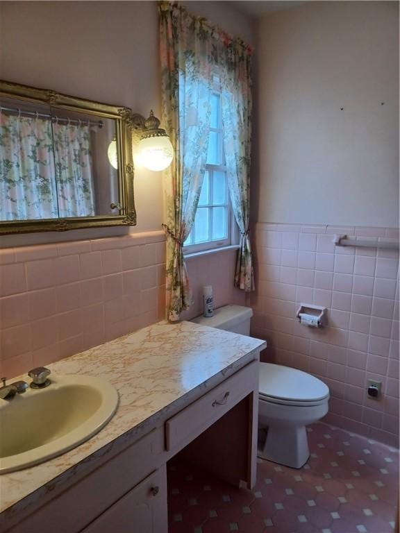 bathroom with a wainscoted wall, toilet, tile walls, and vanity