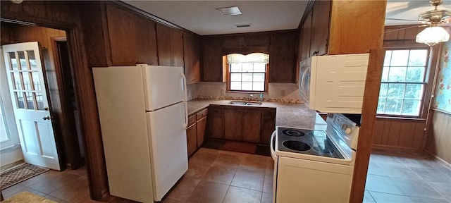 kitchen featuring wood walls, light countertops, light tile patterned floors, white appliances, and a sink