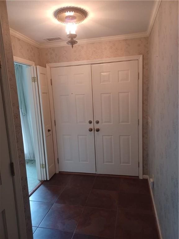 doorway to outside with wallpapered walls, dark tile patterned flooring, visible vents, and ornamental molding