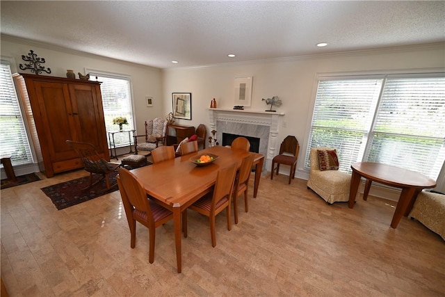 dining space featuring crown molding, light wood-type flooring, a high end fireplace, and a textured ceiling