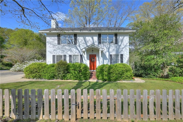 colonial house with a chimney, a fenced front yard, and a front yard