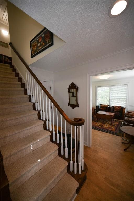 stairway with a textured ceiling, wood finished floors, and ornamental molding