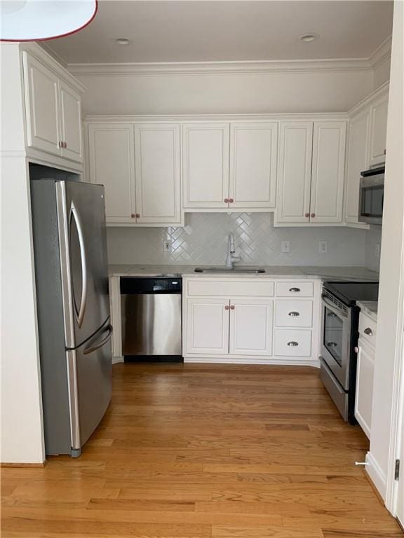 kitchen featuring appliances with stainless steel finishes, a sink, white cabinets, light countertops, and ornamental molding