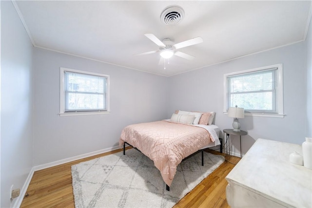 bedroom featuring multiple windows, light hardwood / wood-style floors, ceiling fan, and ornamental molding