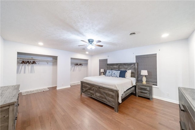 bedroom featuring hardwood / wood-style flooring, ceiling fan, a textured ceiling, and two closets