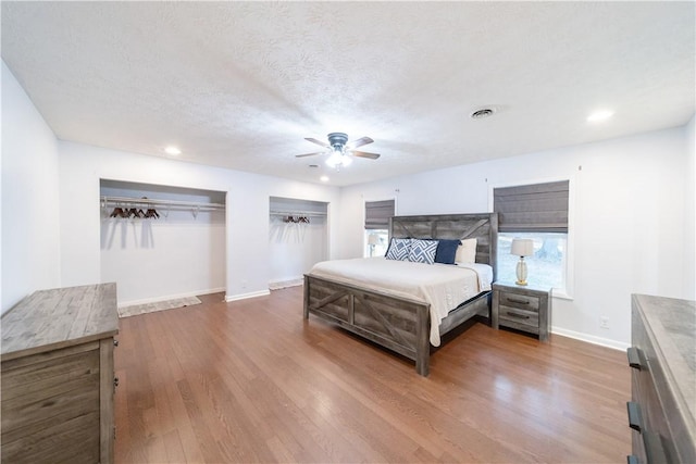 bedroom with hardwood / wood-style floors, ceiling fan, a textured ceiling, and two closets