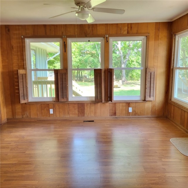 unfurnished room featuring visible vents, wood finished floors, baseboards, ceiling fan, and wooden walls
