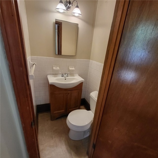 bathroom featuring vanity, a wainscoted wall, toilet, and tile walls