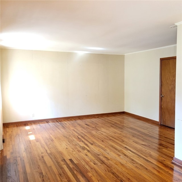 empty room with wood-type flooring, baseboards, and crown molding