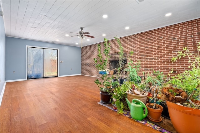 unfurnished living room featuring brick wall, wood finished floors, a ceiling fan, and baseboards