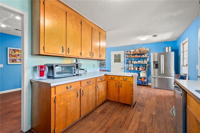 kitchen with appliances with stainless steel finishes, dark wood-style flooring, a peninsula, light countertops, and a textured ceiling