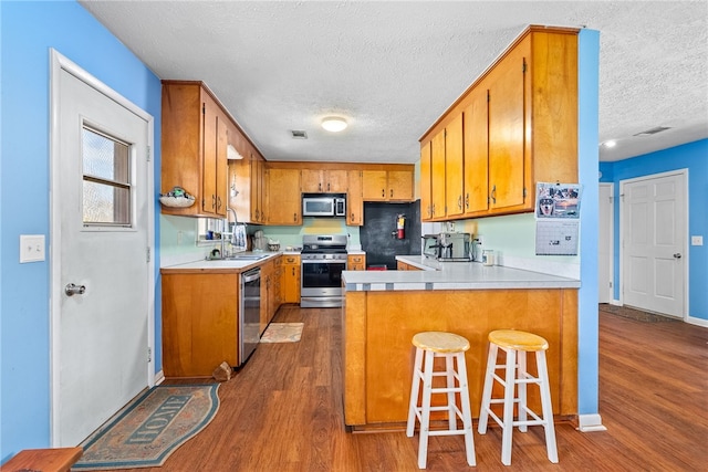 kitchen featuring stainless steel appliances, a peninsula, light countertops, and brown cabinets