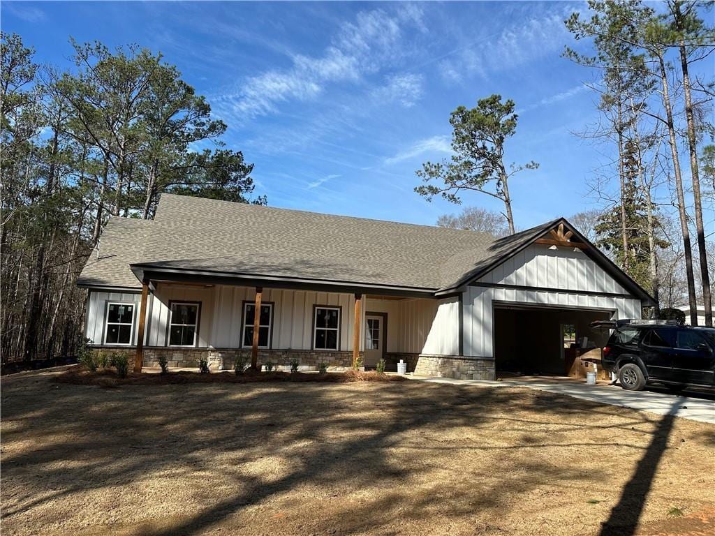 view of front facade with stone siding, roof with shingles, driveway, and an attached garage