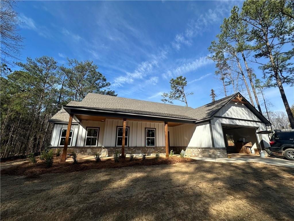 modern farmhouse featuring covered porch, board and batten siding, a garage, stone siding, and driveway