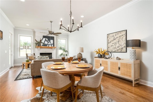 dining area with a fireplace, wood-type flooring, ceiling fan with notable chandelier, and crown molding