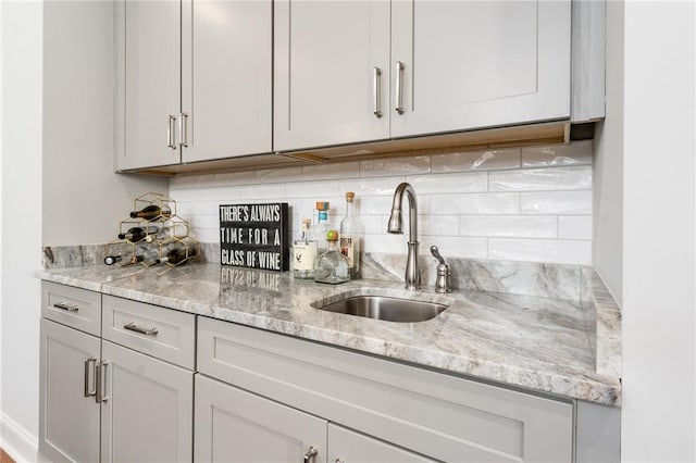 kitchen featuring decorative backsplash, light stone counters, and sink