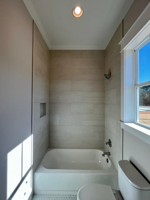 bathroom featuring ornamental molding, tiled shower / bath combo, and toilet