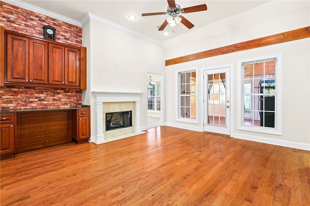 unfurnished living room featuring light wood-style flooring, ornamental molding, a ceiling fan, a tile fireplace, and baseboards