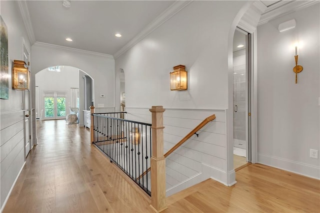 corridor featuring wood finished floors, an upstairs landing, crown molding, baseboards, and arched walkways