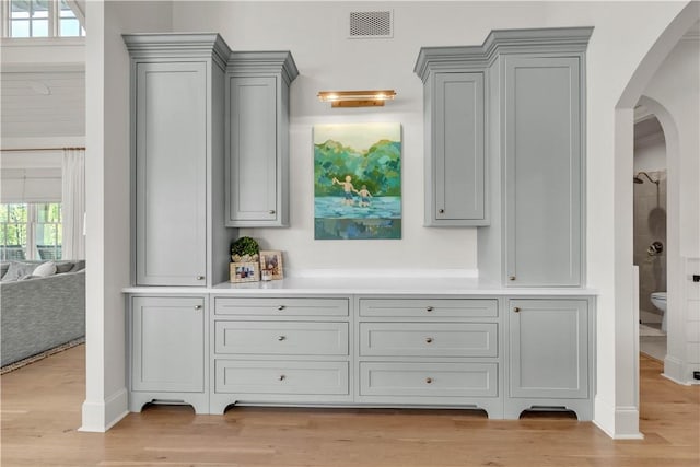 bar featuring arched walkways, baseboards, visible vents, and light wood-type flooring