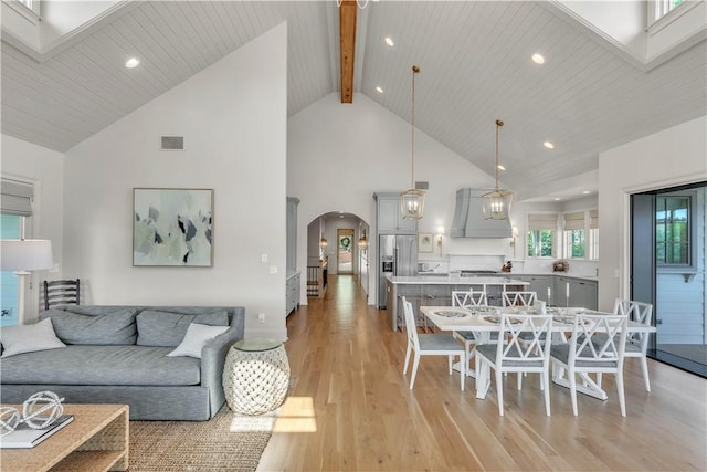 living room featuring light wood-style floors, visible vents, arched walkways, and high vaulted ceiling