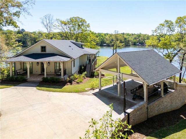 exterior space with a porch, roof with shingles, driveway, a carport, and a water view