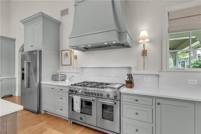 kitchen with gray cabinets, visible vents, premium appliances, light wood-style flooring, and custom range hood