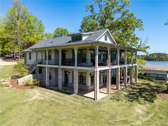 back of property with a yard, a balcony, a water view, a patio area, and a shingled roof