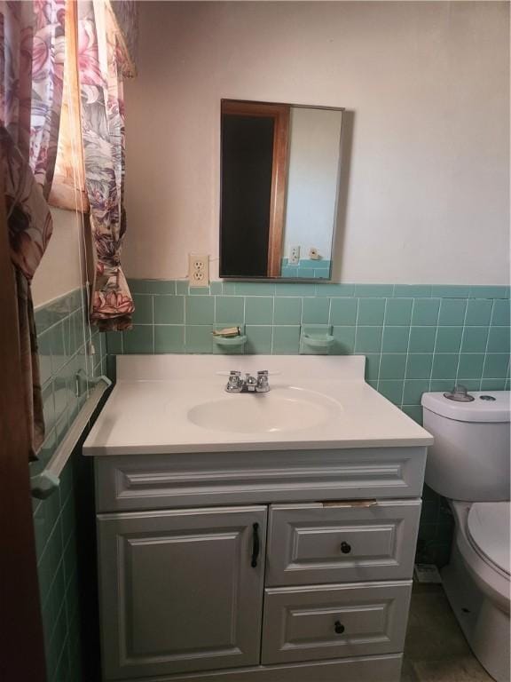 bathroom featuring wainscoting, vanity, toilet, and tile walls