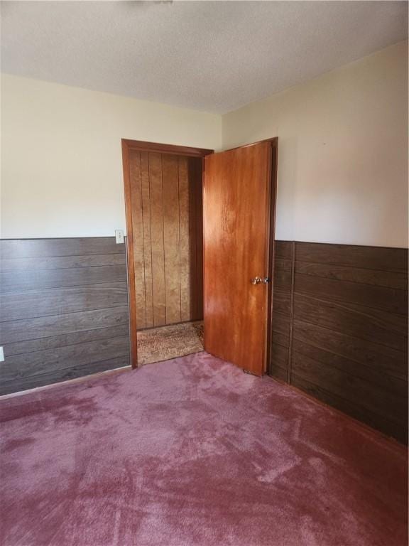 carpeted spare room with wood walls, a textured ceiling, and a wainscoted wall