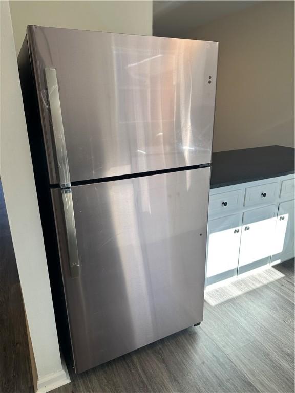 interior details with stainless steel fridge, white cabinetry, and dark wood-type flooring