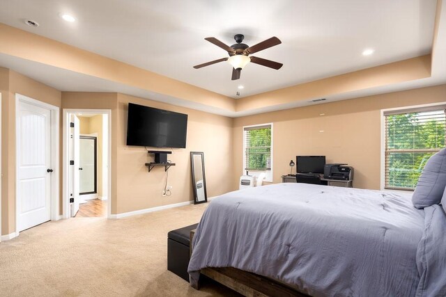 bedroom featuring a tray ceiling, light colored carpet, and ceiling fan