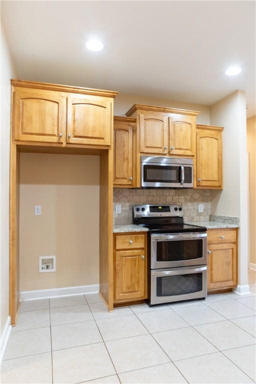 kitchen with decorative backsplash, light stone countertops, light tile patterned floors, and stainless steel appliances