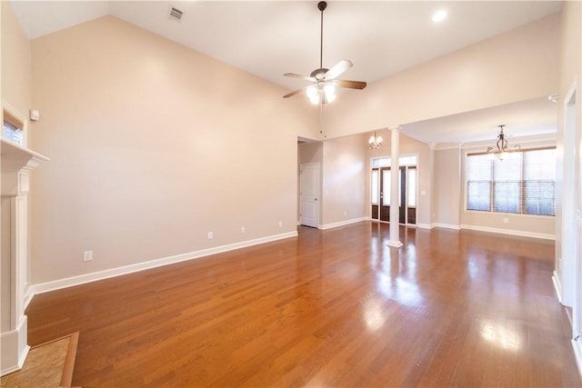 unfurnished living room featuring ceiling fan with notable chandelier, dark hardwood / wood-style flooring, decorative columns, and high vaulted ceiling